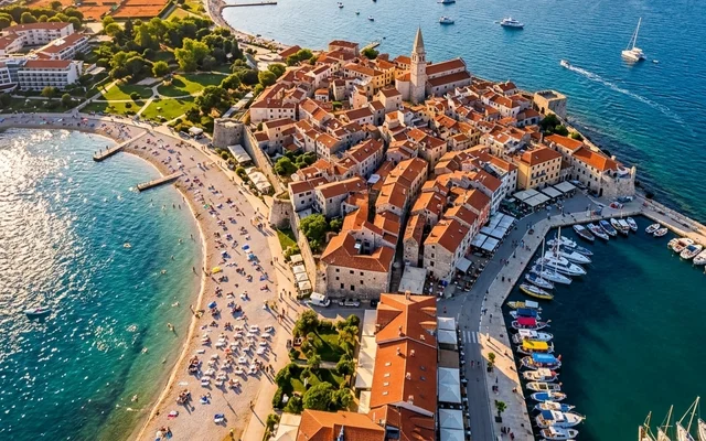 Umag iz vazduha — staro jezgro s crvenim krovovima na poluostrvu, peščana plaža sa suncobranima i marina, istarska obala Jadrana, Hrvatska